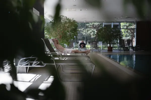 Blick durch Blätter auf Liegen und Mann im Badetuch neben Pool und Garten im Manhattan Club Brunn
